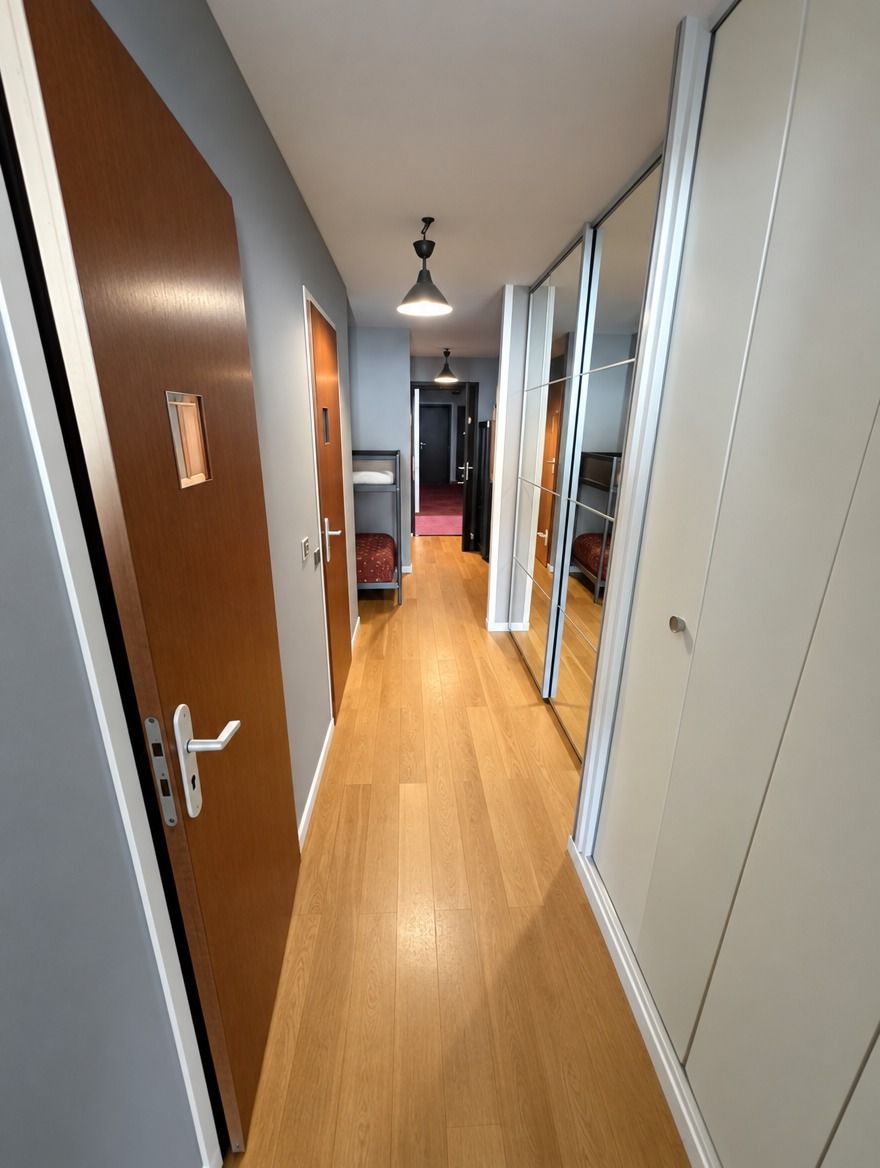 A hallway with wooden flooring, a ceiling fan, and sliding doors leading to a room with a bed.