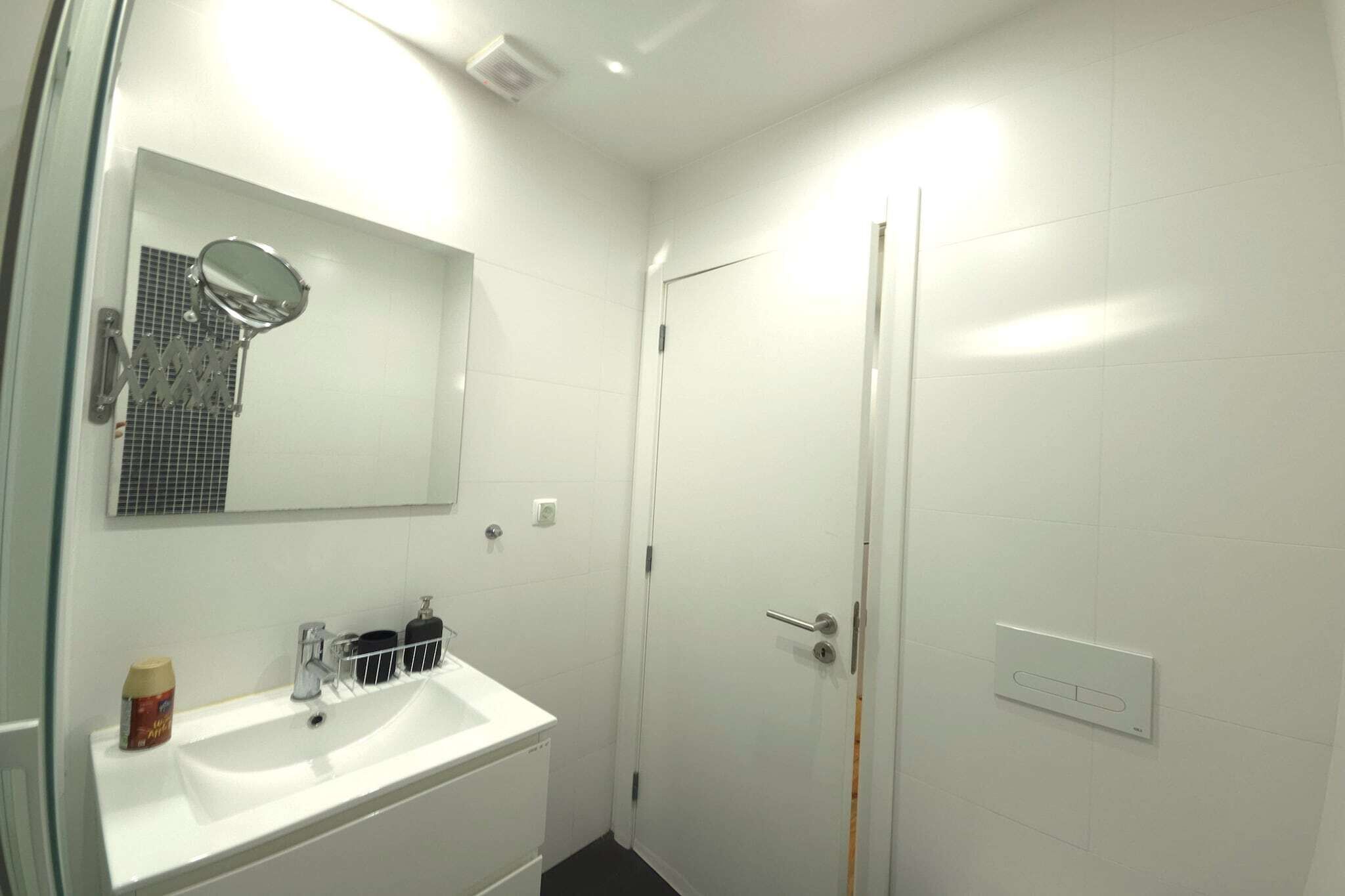 Une salle de bain avec un lavabo blanc, un miroir et une porte.