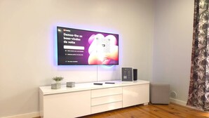 Uma sala de estar moderna com televisão de tela plana na parede, uma mesinha console branca com uma pequena planta e uma cortina estampada.