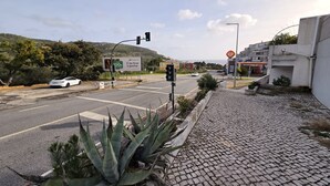 Cruzamento de rua com um carro branco, semáforos e uma placa.