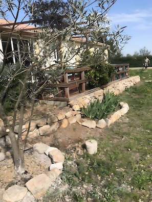 Un jardín con un porche de madera, un camino de piedra y un pequeño estanque.