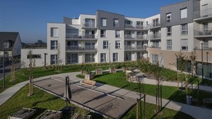 A modern apartment complex with multiple balconies, a central courtyard with seating, and a well-maintained garden.