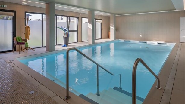 An indoor swimming pool with clear water, a tiled floor, and a chair with a towel.