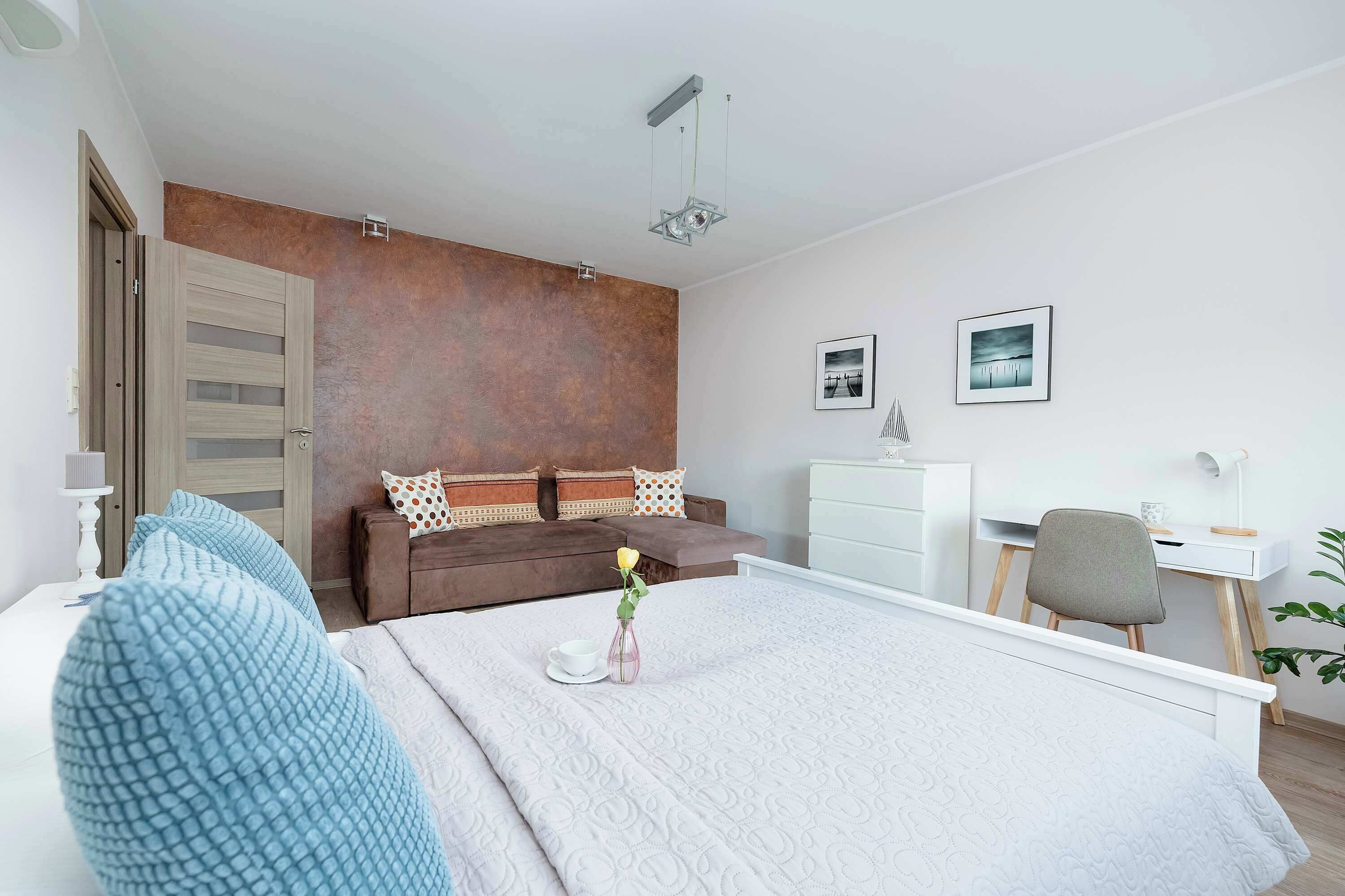 Un dormitorio moderno con una cama grande, un sofá marrón, un escritorio y una silla.