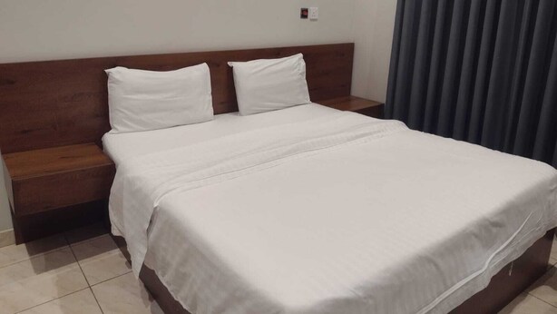Ein ordentlich bezogenes Bett mit weißer Bettwäsche in einem Zimmer, das ein Holz-Kopfteil und einen Nachttisch hat.