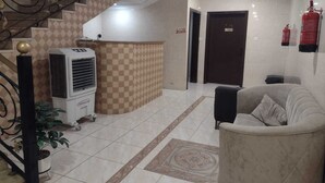 Eine Lobby mit Schachbrettmuster an der Wand, einer Treppe, einem Empfangstisch, einem Feuerlöscher und einem Sofa.