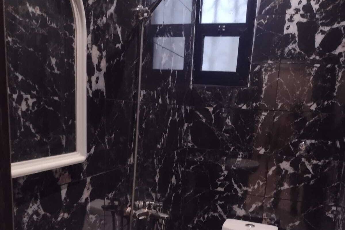 A bathroom with a marble floor, a white sink, a toilet, and a shower with a handheld showerhead.