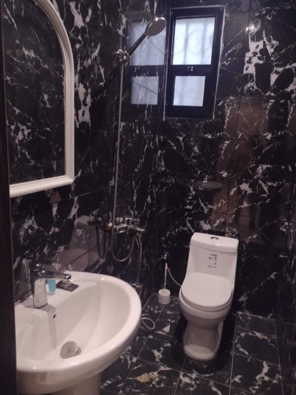 A bathroom with a marble floor, a white sink, a toilet, and a shower with a handheld showerhead. - Bussmaa swet (Riyadh)