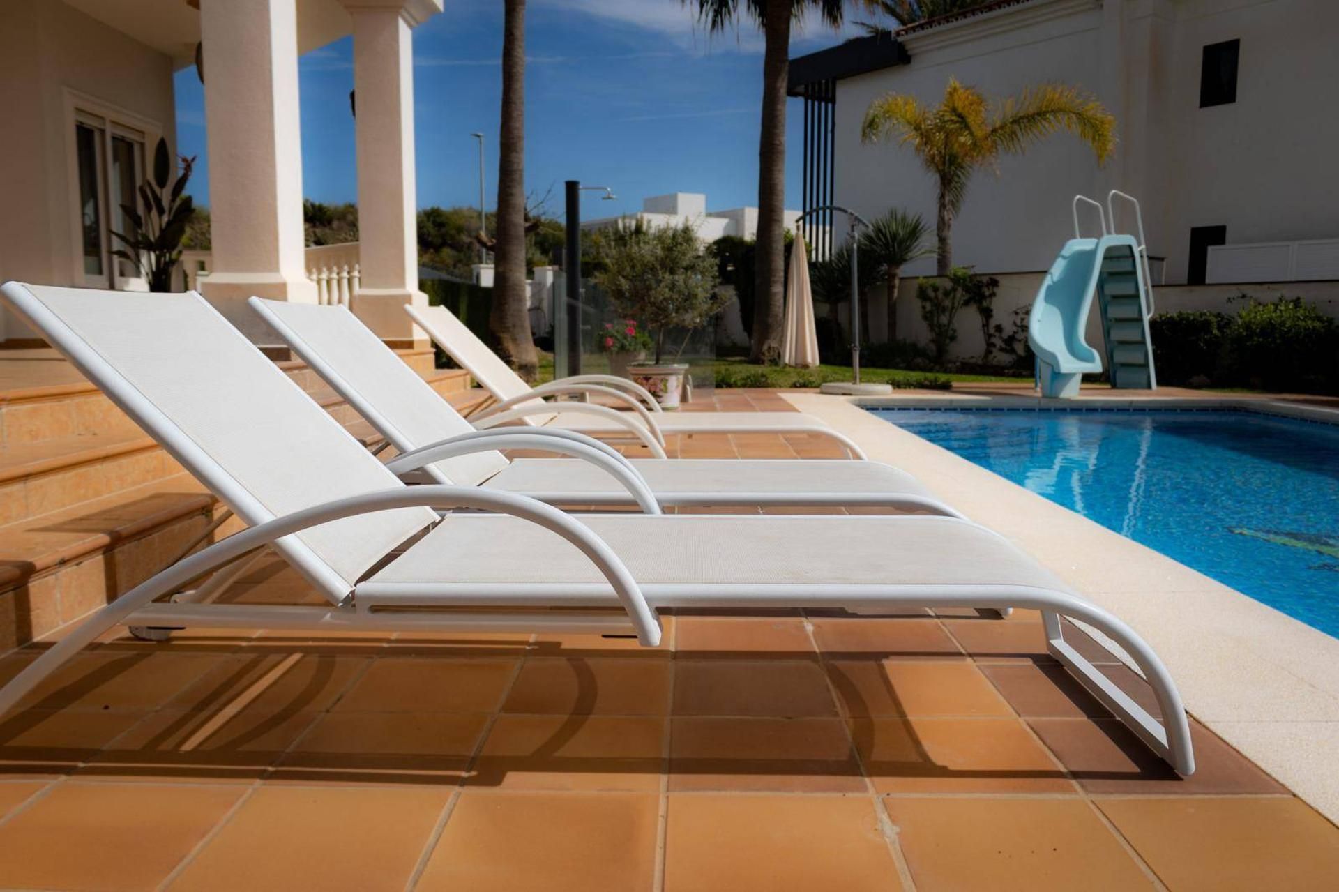Zona de piscina amb gandules blanques i un tobogan blau.