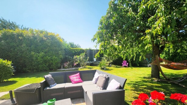 A patio area with a wicker sofa set, a green watering can, and red flowers. - Premium Suite near CDG Airport and Parc Astérix (Villeron)