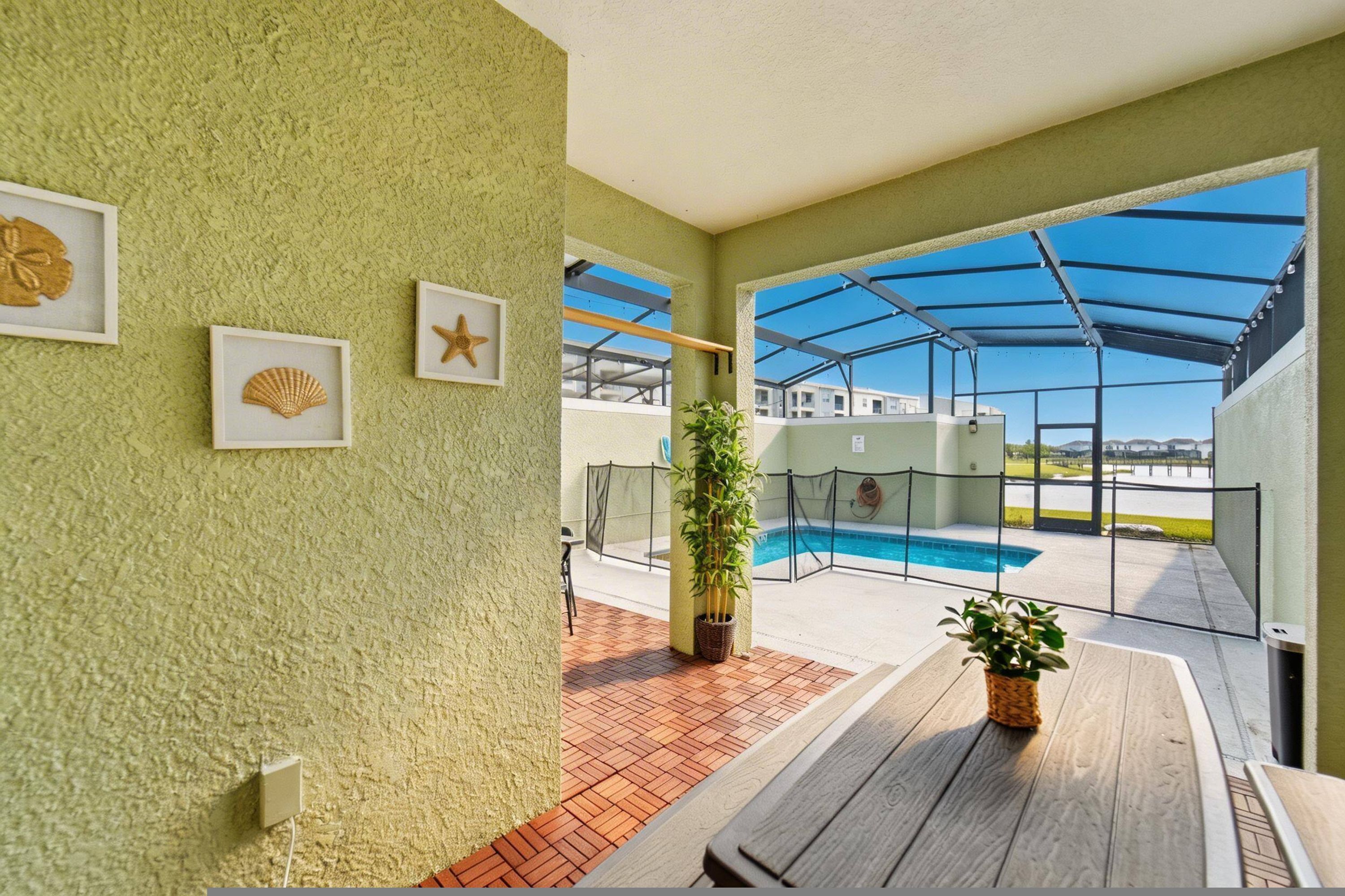 A poolside area with a covered patio, a wooden table, and framed sea shells on the wall.