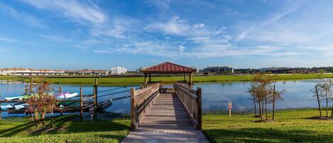 A wooden boardwalk leading to a gazebo over a calm lake, with boats docked nearby.