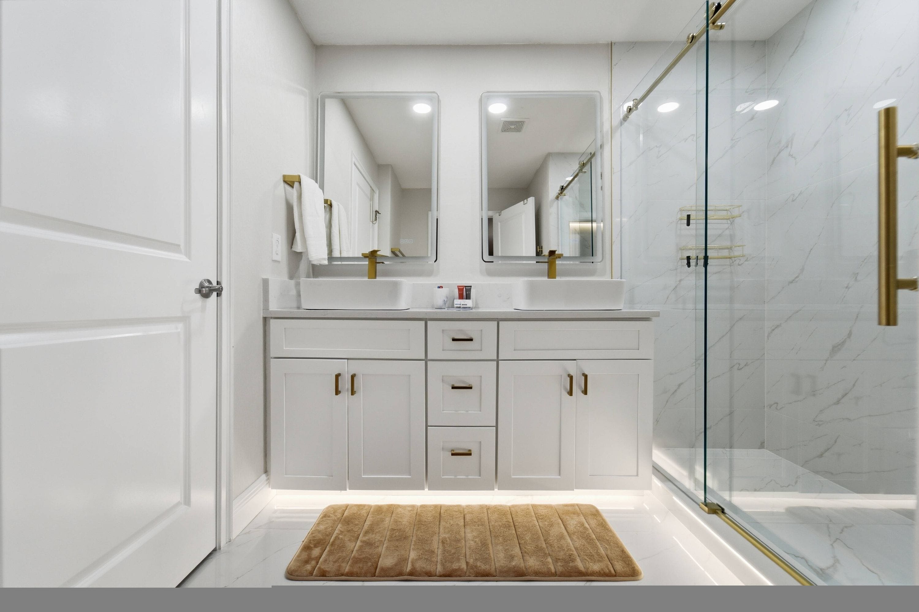 Un baño moderno con cabina de ducha de vidrio, muebles de color blanco y un espejo grande sobre el lavabo.