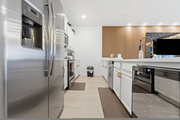 A modern kitchen with stainless steel appliances, white cabinetry, and a wooden accent wall. - 4BR Home at Storey Lake Near Disney (Kissimmee)