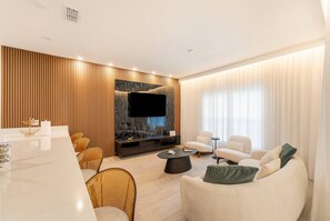 Un soggiorno moderno con televisione a schermo piatto, divani bianchi, un tavolo da pranzo e un pannello decorativo a parete.