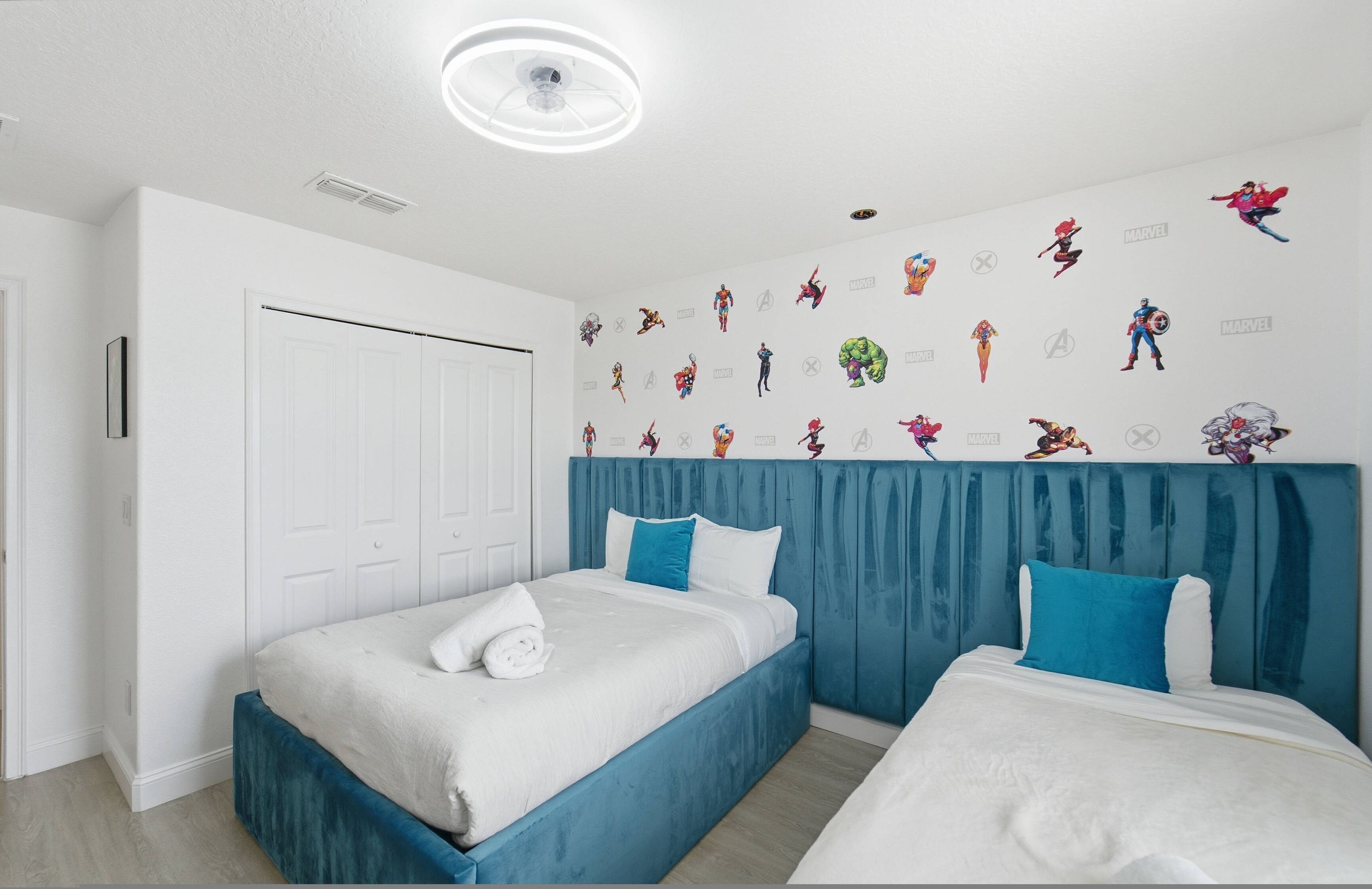 Habitación de hotel con dos camas, una puerta blanca y una pared decorada con personajes de Marvel.