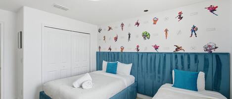 Habitación de hotel con dos camas, una puerta blanca y una pared decorada con personajes de Marvel.
