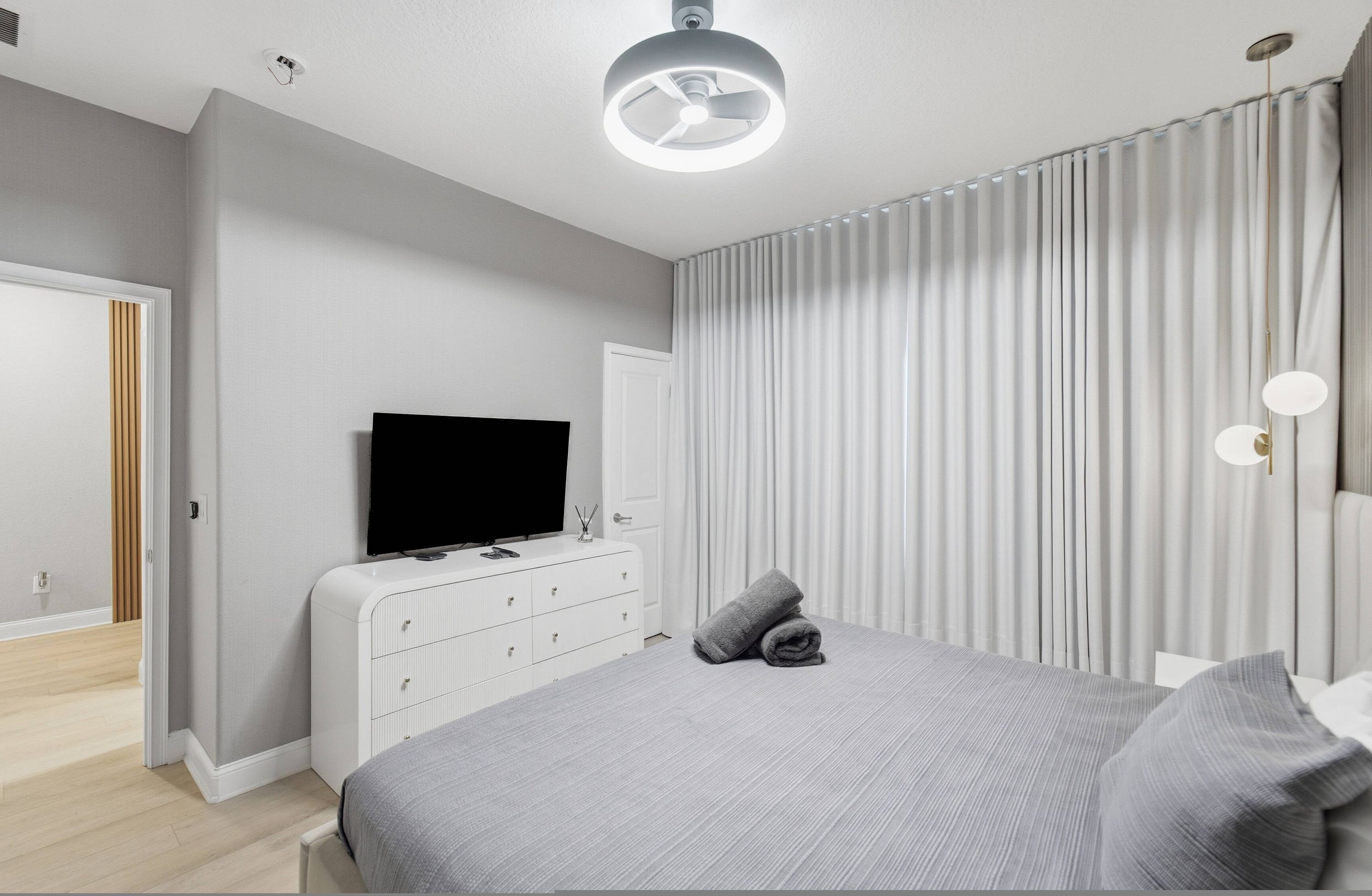 A modern bedroom with a large bed, a flat-screen TV, a dresser, and a ceiling light fixture.