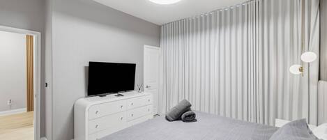 Un dormitorio moderno con una cama grande, un televisor de pantalla plana, un aparador y una lámpara en el techo.