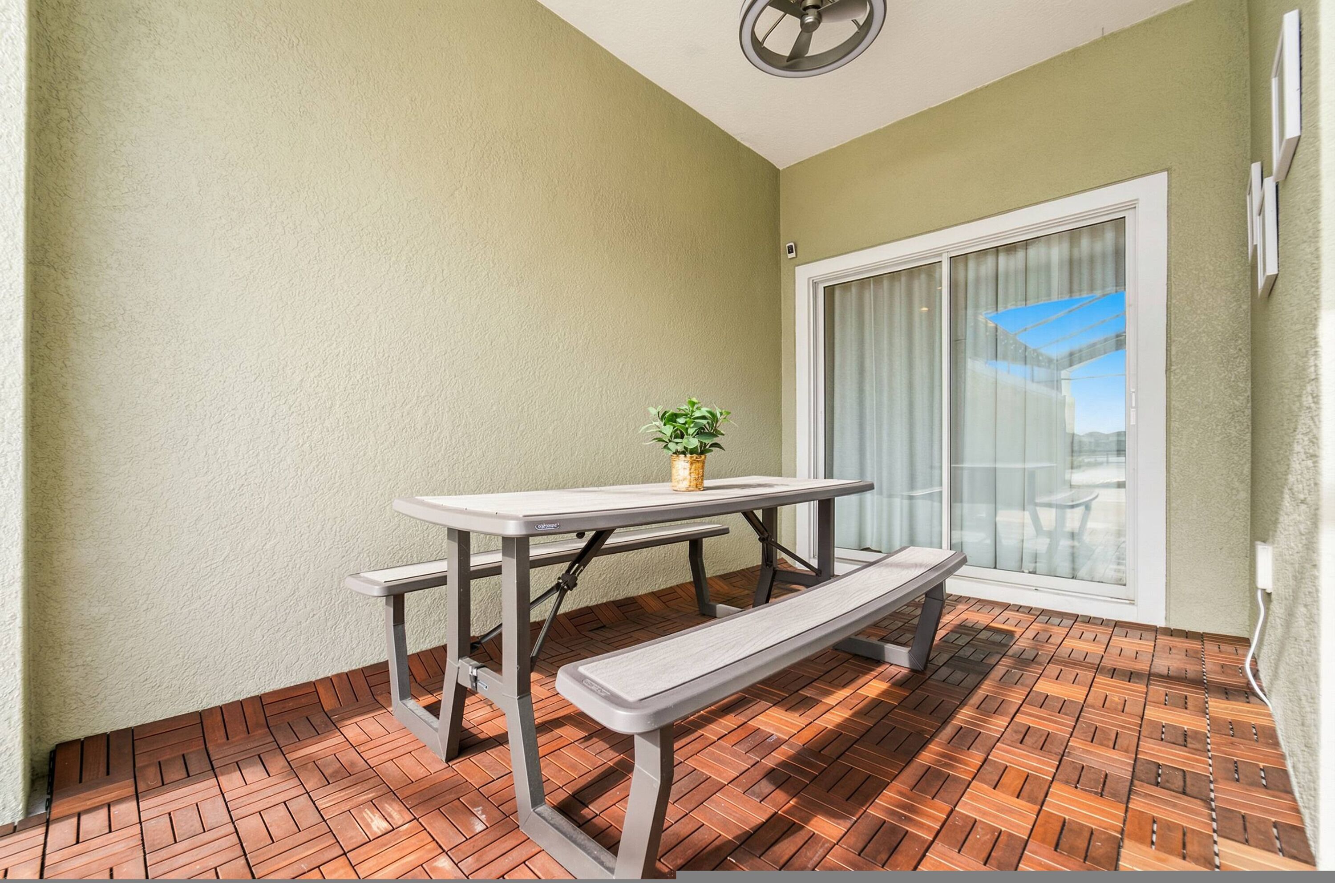 Un patio con una mesa, un banco, una planta en maceta y un ventanal corredero.