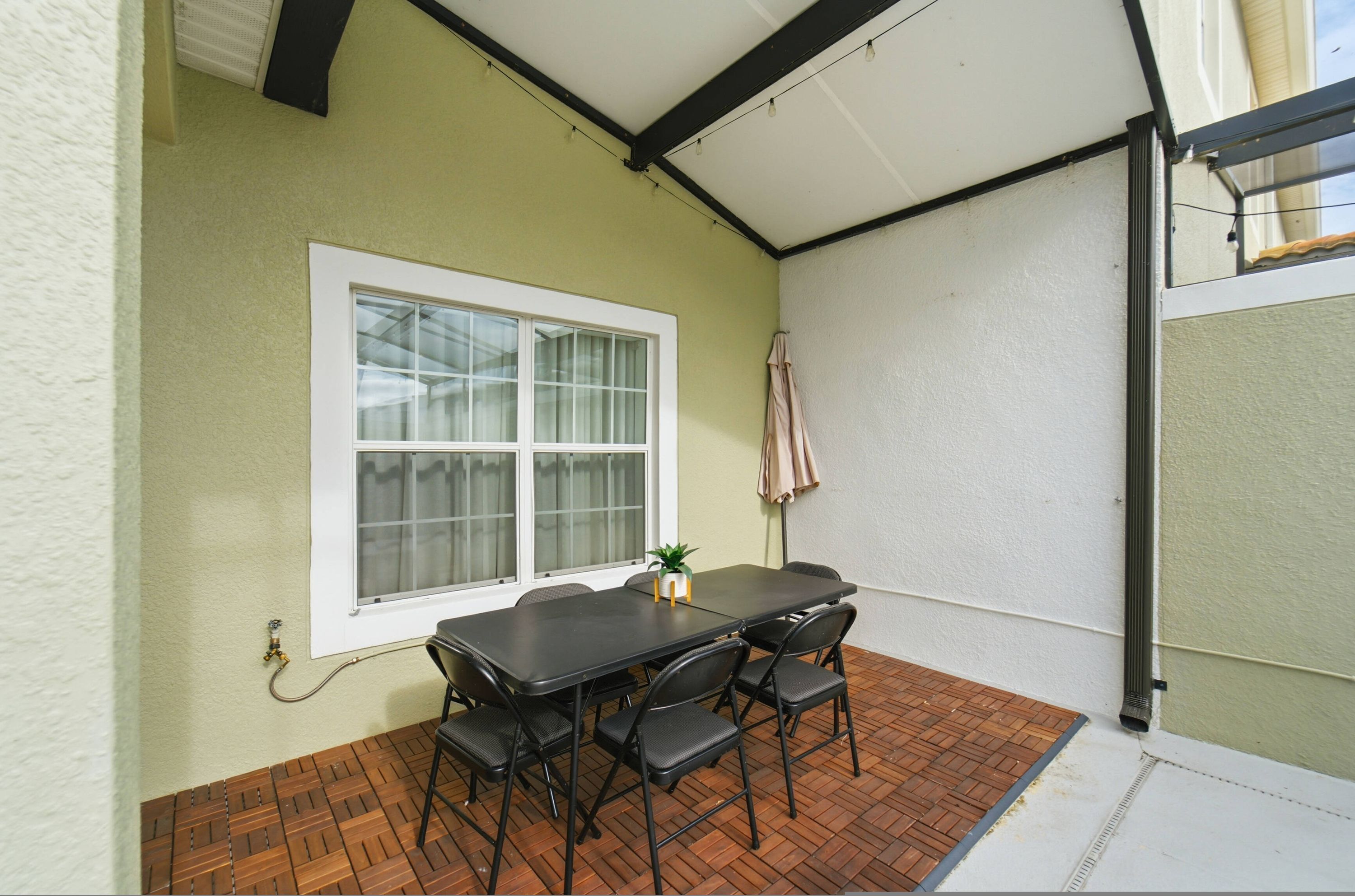 A patio with a table and chairs, a window, and a small plant.