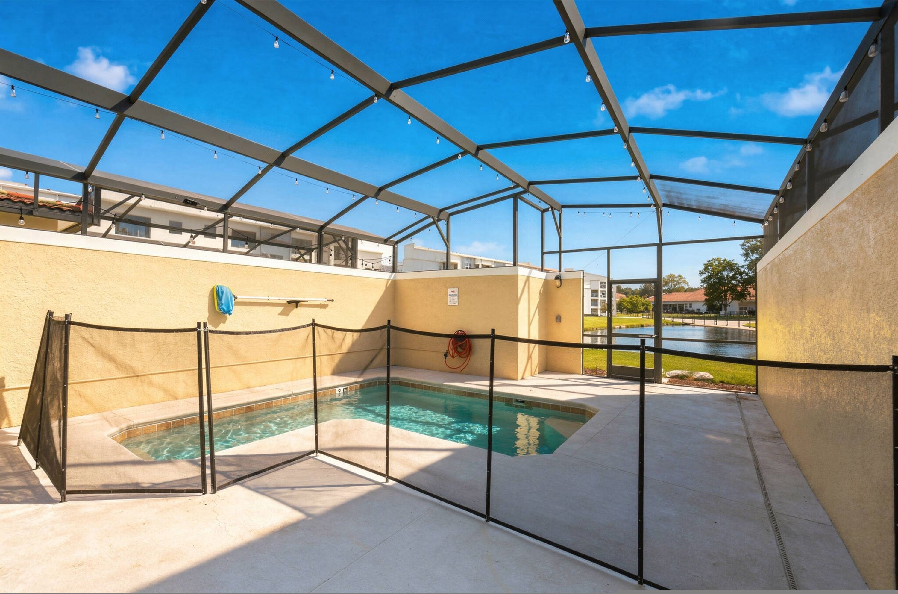 Une piscine extérieure couverte, dotée d’un toit en métal, entourée d’une clôture, et un espace aménagé au bord de la piscine avec un tuyau d’arrosage.