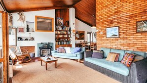 Een gezellige woonkamer met een open haard, een blauwe bank en een houten plafond.