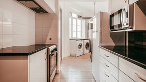Une cuisine moderne équipée d’un four encastré, d’un four à micro-ondes et d’un lave-linge, avec des meubles de couleur claire et un plancher en bois.