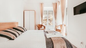 Une chambre à coucher avec un lit, un téléviseur fixé au mur et une fenêtre avec des rideaux.