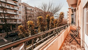 Un balcon doté d’une rambarde en métal, d’un sol carrelé et offrant une vue sur une rue bordée de voitures garées et d’immeubles.