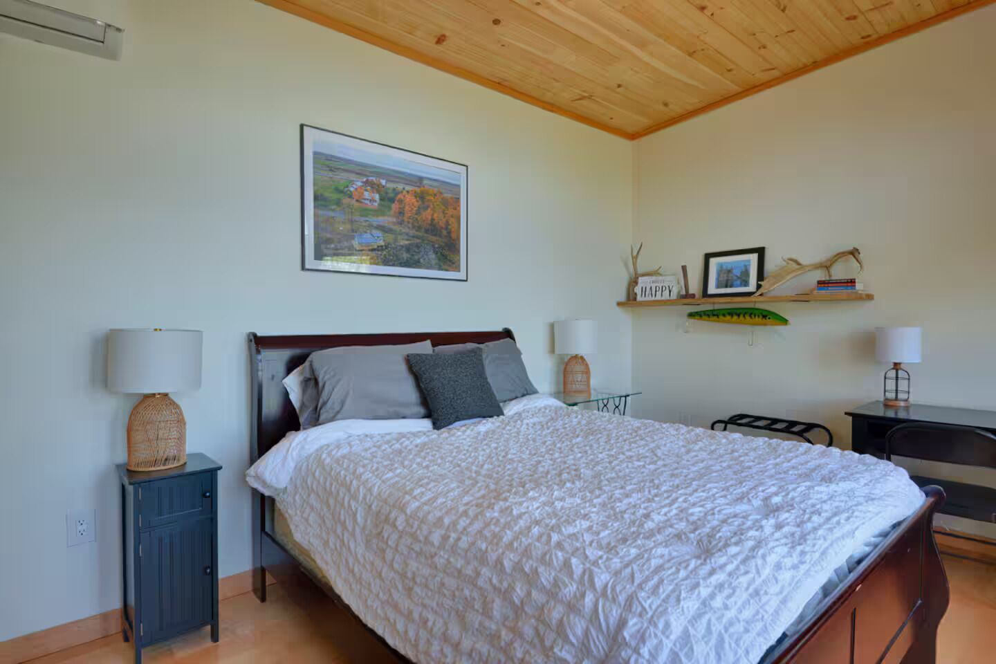 Un dormitorio con cama, mesitas de noche, un escritorio y una estantería con adornos.