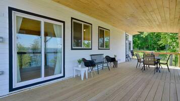 A covered outdoor deck with a wooden floor and a railing, featuring a table and chairs, and large sliding glass doors.