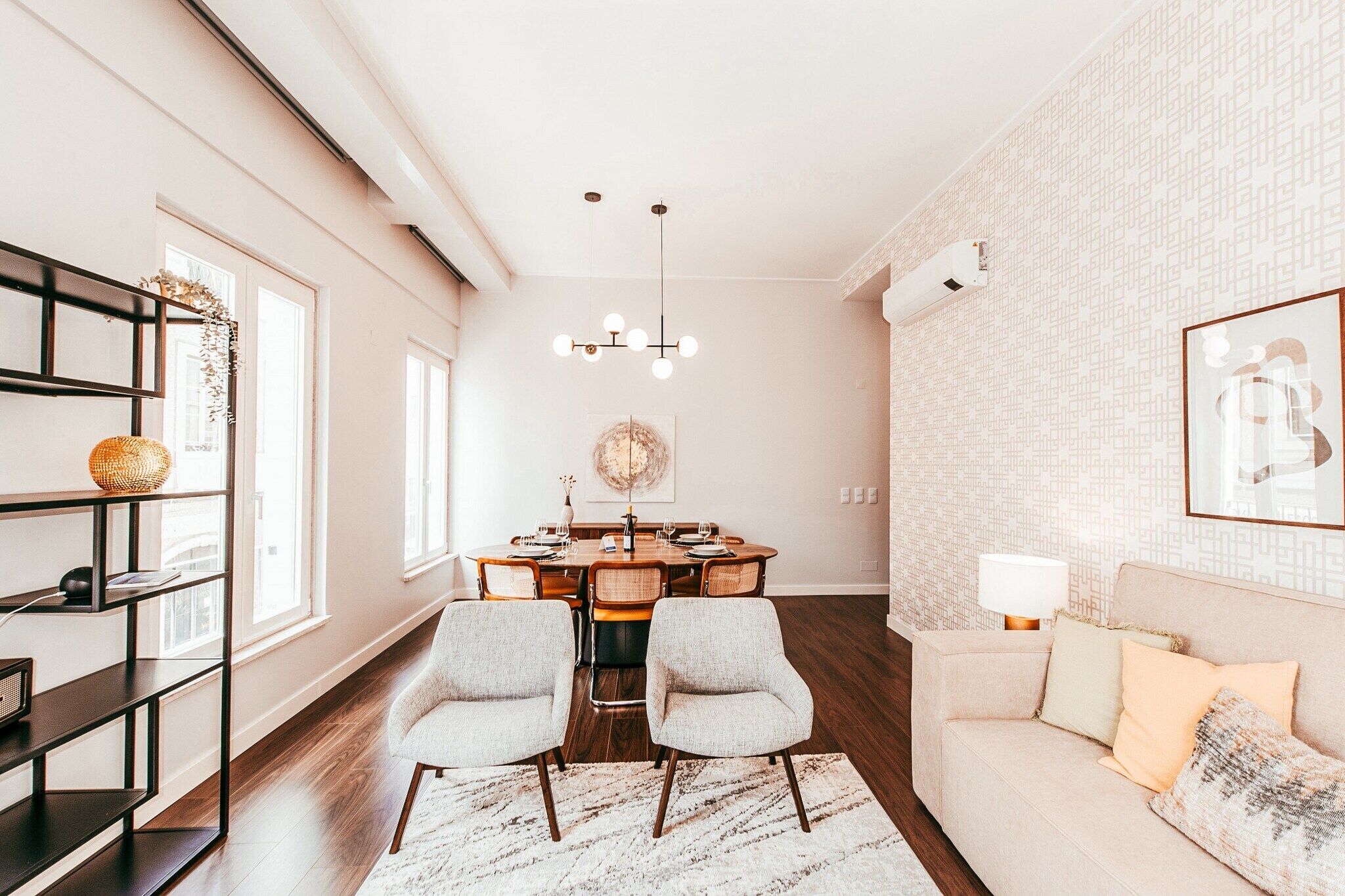 A modern living room with a dining area, featuring a round table, two armchairs, a sofa, and a bookshelf.