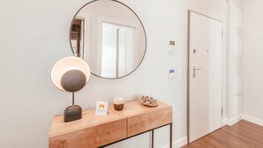 En minimalistisk hall med ett konsolbord i trä, en rund spegel, en vägglampa och en dörr.
