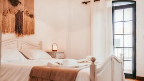 Ein ordentlich bezogenes Bett mit Kopfteil, ein Nachttisch mit Lampe und eine an der Wand hängende Makramee-Dekoration.