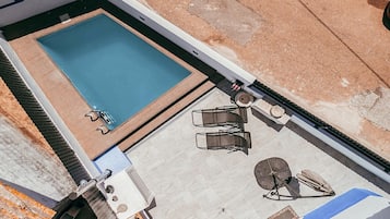 Eine Vogelperspektive zeigt einen Poolbereich auf einem Dach, mit einem rechteckigen Pool, zwei Liegestühlen und einem kleinen Tisch.