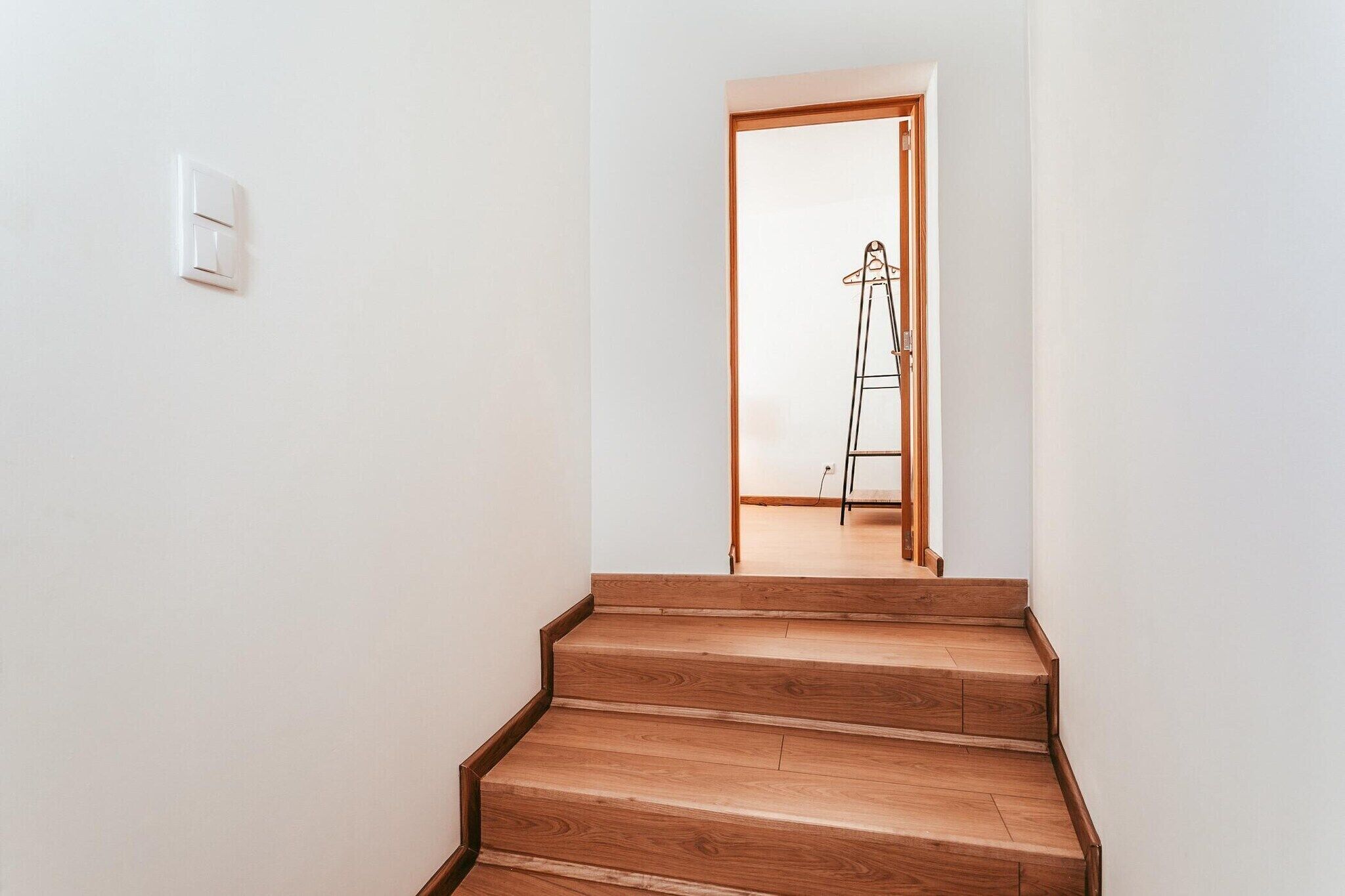 Un escalier menant à une pièce dotée d’un plancher en bois et d’un mur blanc.