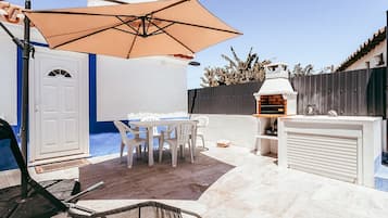 Eine Terrasse im Freien mit Tisch, Stühlen und einem Grill. Eine weiße Tür ist ebenfalls zu sehen.