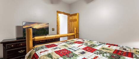A bedroom with a wooden bed frame, a quilt, a dresser, a television, and a ceiling fan.