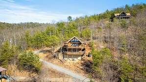 A two-story log cabin with a balcony, surrounded by dense forest and a dirt road. - Edge of Glory Cabin | Views | Hot Tub | BBQ (Pigeon Forge)