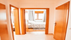 Un pasillo estrecho que da a un dormitorio con cama, cortinas y ventana.