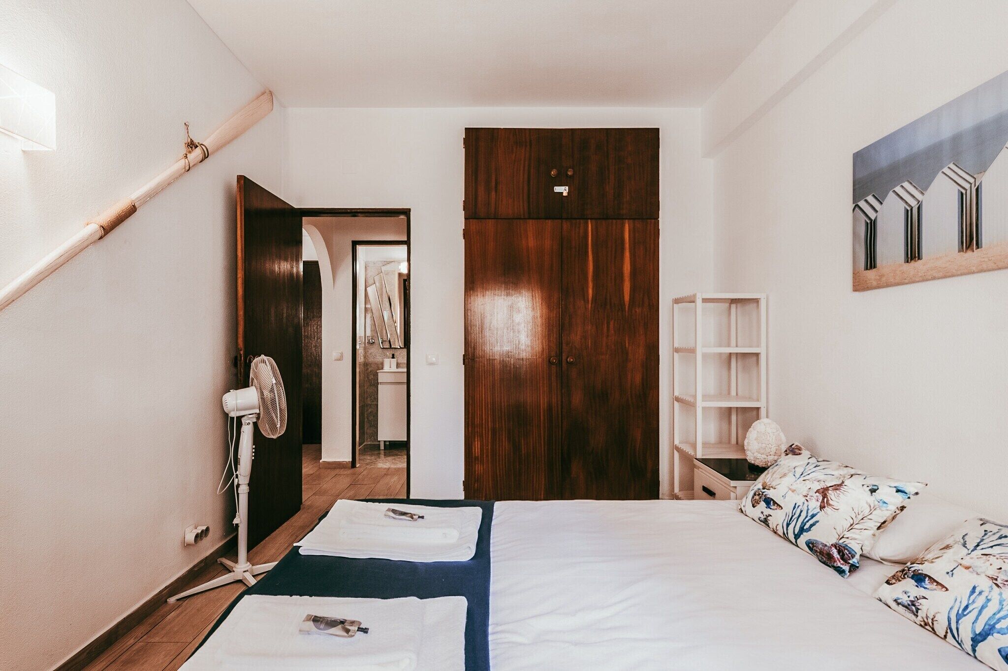 Una camera da letto con un letto, un armadio in legno, un ventilatore e una mensola con oggetti decorativi.