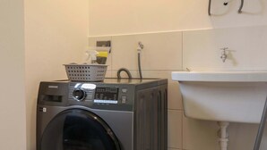 A compact laundry room with a front-loading washing machine, a wall-mounted heater, and a sink. - w* | Engaging Loft in the Heart of San Isidro (San Isidro)