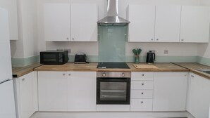 Eine kompakte Küche mit weißen Schränken, einer Edelstahl-Dunstabzugshaube, einer Mikrowelle, einem Toaster und einem eingebauten Backofen.