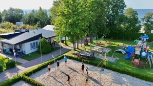 A sandy volleyball court with players, a playground, and a building with a sloped roof. - Holiday home very close to the beach (Sianozety)