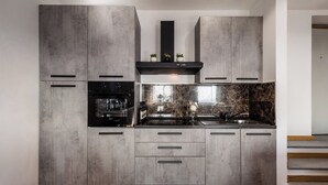 Una cocina moderna con armarios grises, un horno negro, un protector contra salpicaduras de mármol y una planta pequeña en la encimera.