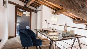 Un dormitorio estilo loft moderno con vigas de madera a la vista, una mesa de vidrio con lámpara y una silla azul oscuro.