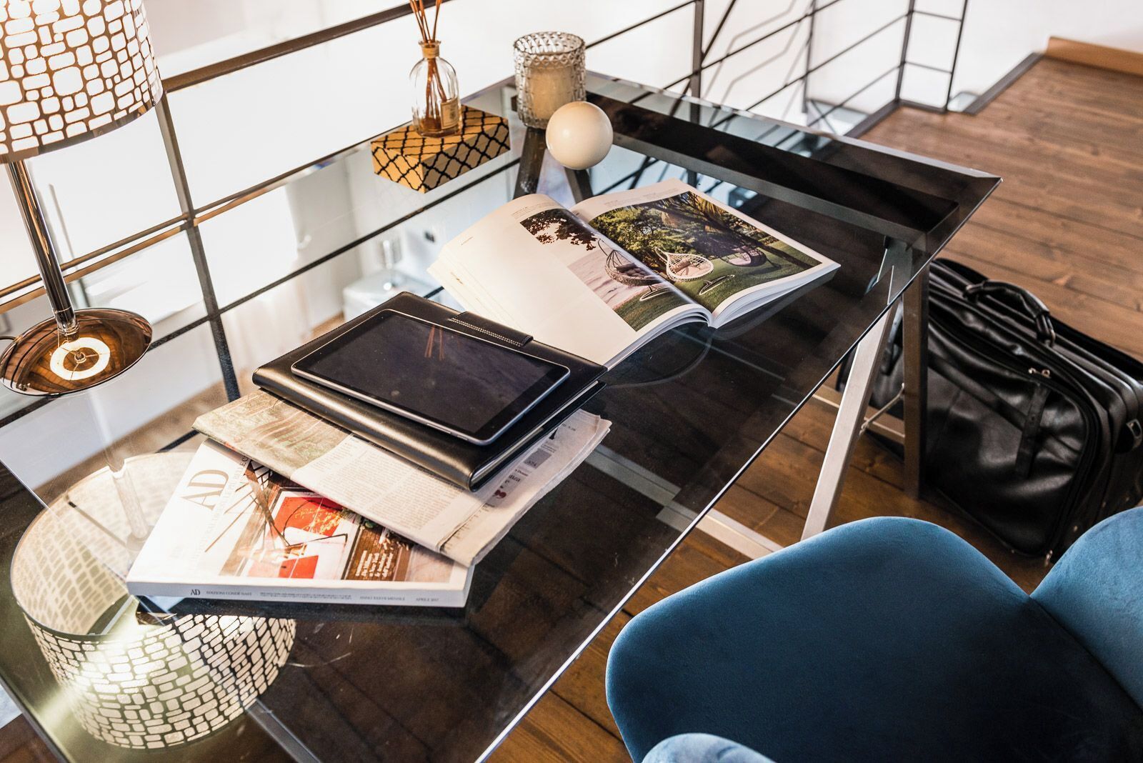 Una habitación moderna con una mesa de centro de vidrio, una tableta, revistas y un bolso de cuero negro.