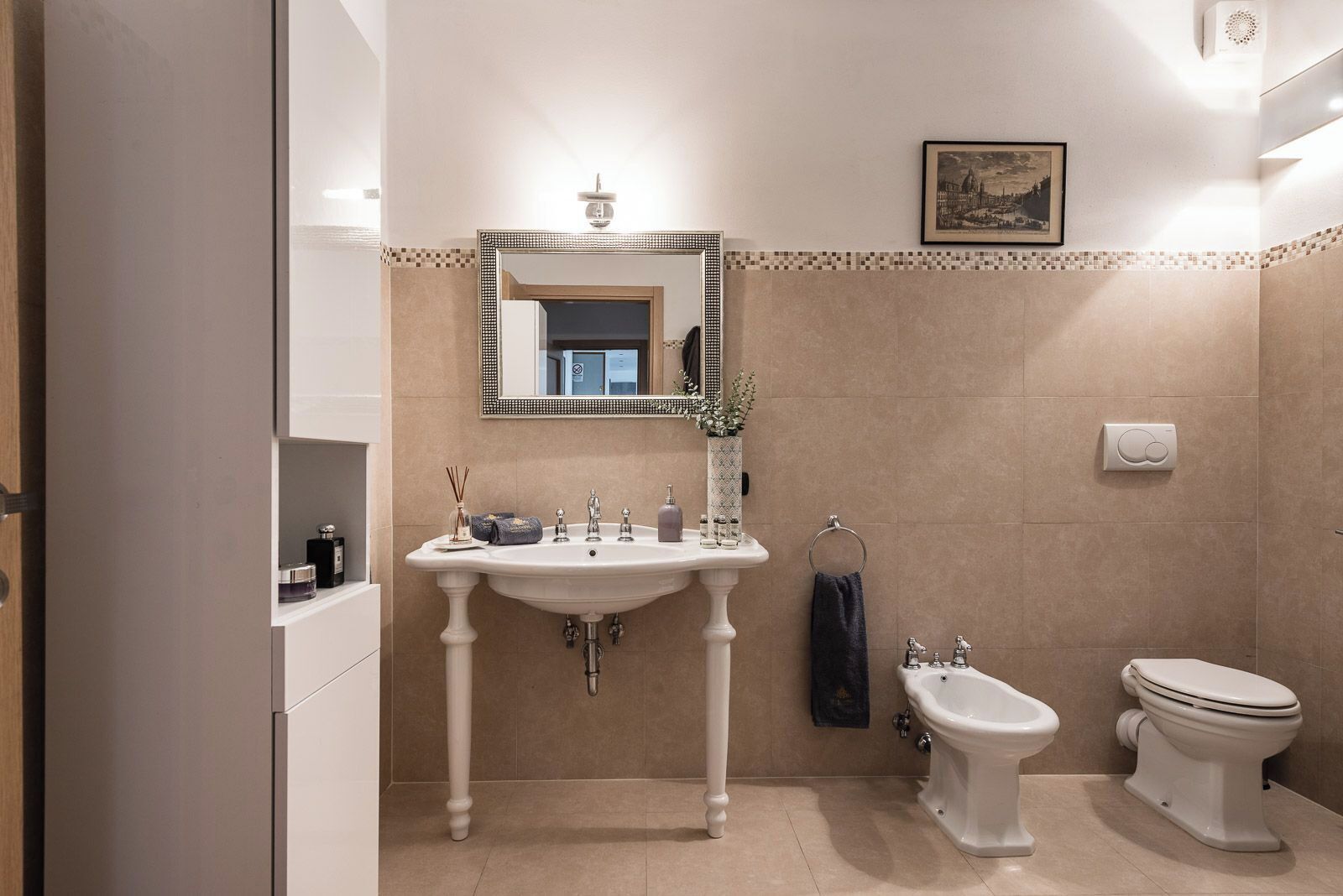 Un baño con lavamanos pedestal, un bidé, un inodoro y un espejo con marco decorativo.