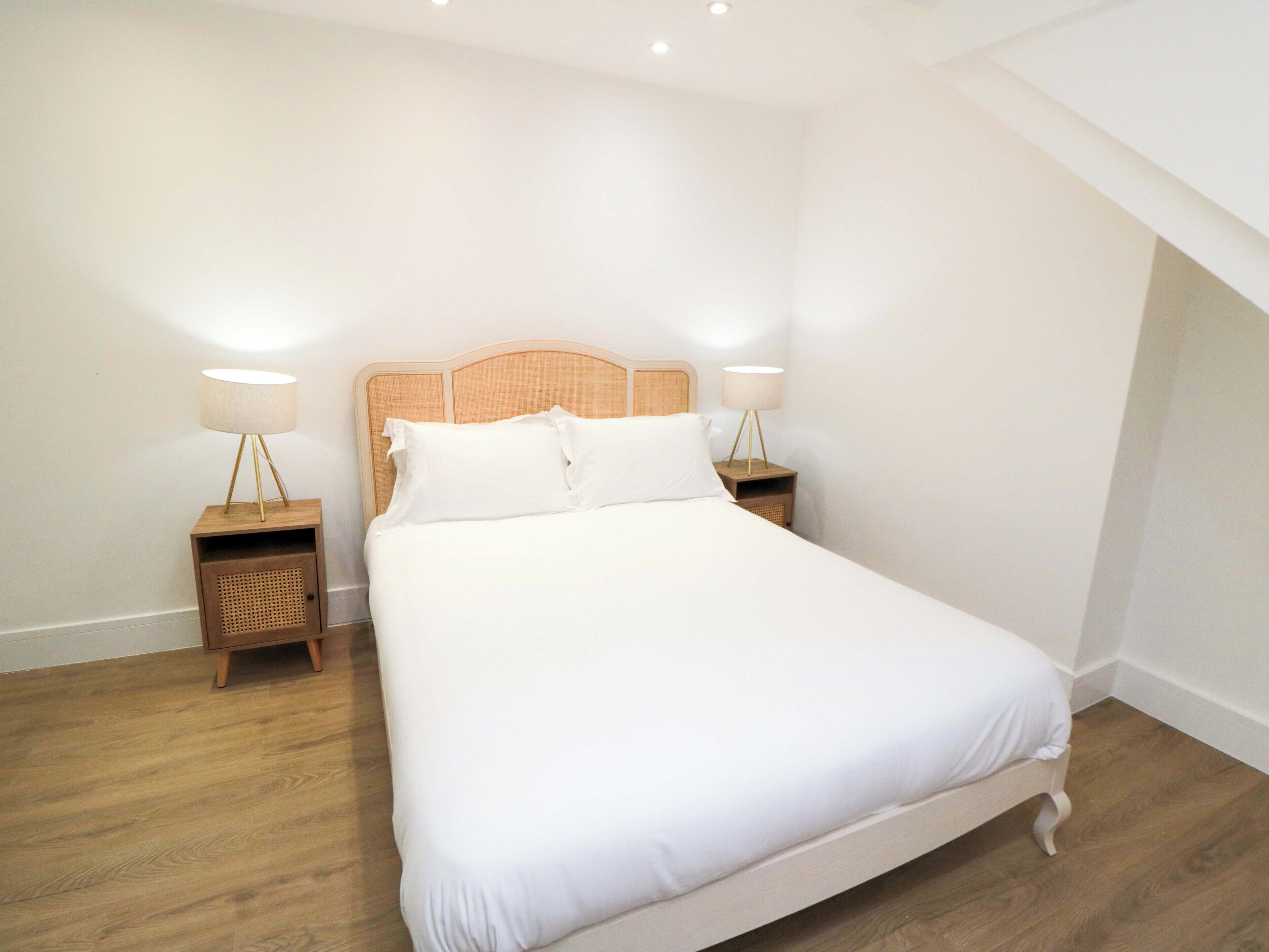 Ein ordentlich eingerichtetes Schlafzimmer mit einem hölzernen Kopfende, zwei Nachttischen mit Lampen und einem großen Bett mit weißer Bettwäsche.